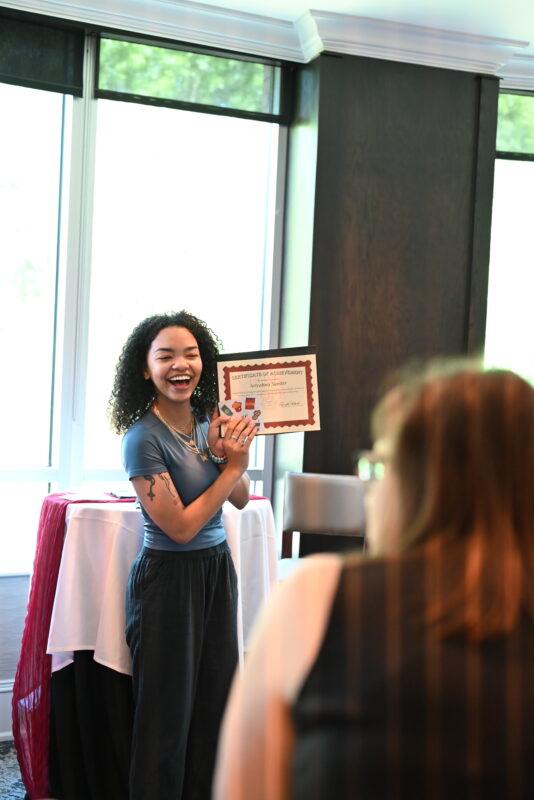 Ari, HOH staff member holding a certificate and smiling.